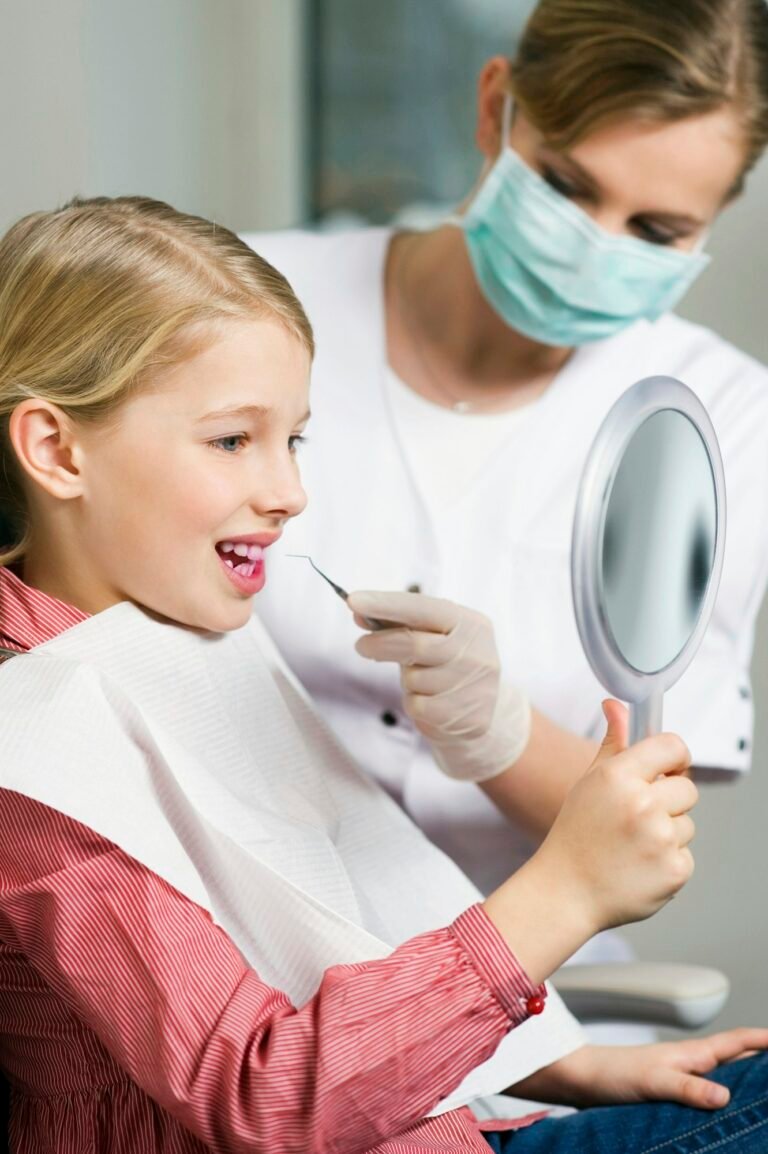 Young girl at the dentist getting a checkup while holding a mirror.